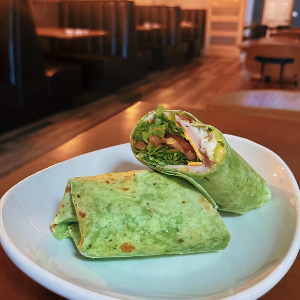 Two green wraps, one cut open to show turkey, cheese, lettuce, and tomato, on a white plate.