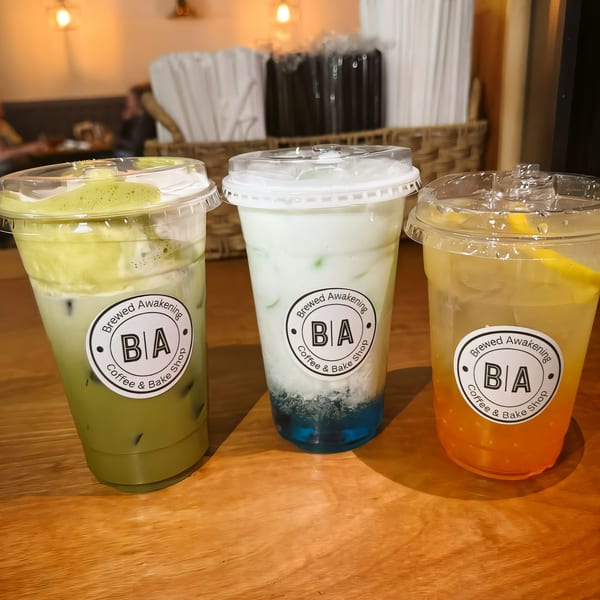 Three colorful iced drinks from Brewed Awakening Coffee & Bake Shop on a wooden table.