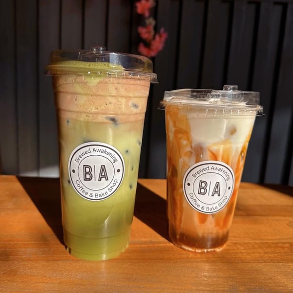Two iced coffee drinks from Brewed Awakening, one green matcha and one caramel, on a wooden table.