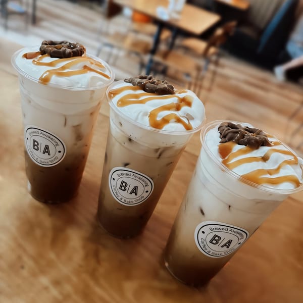 Three iced coffees from Brewed Awakening, topped with whipped cream, caramel drizzle, and chocolate.