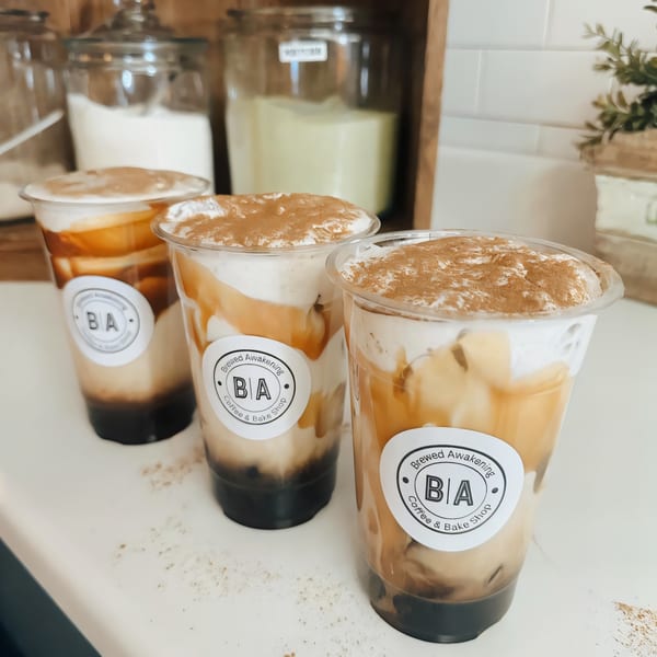 Three iced coffee drinks from Brewed Awakening Coffee and Bake Shop, topped with whipped cream and cinnamon.