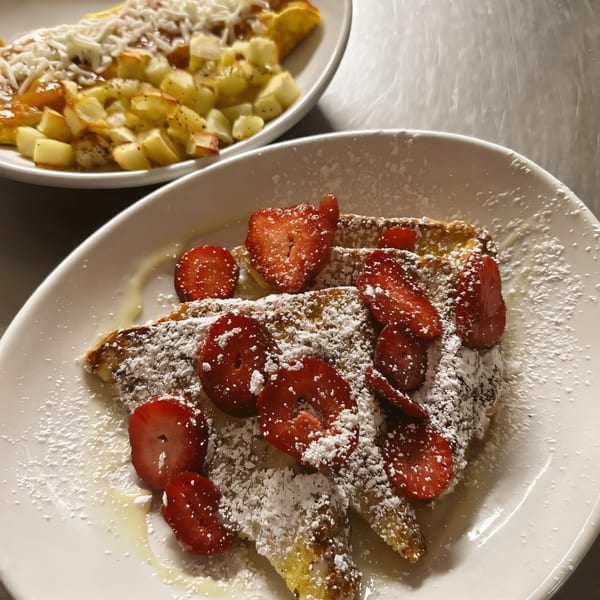 French toast with strawberries and powdered sugar, with a side of potatoes and an omelet.